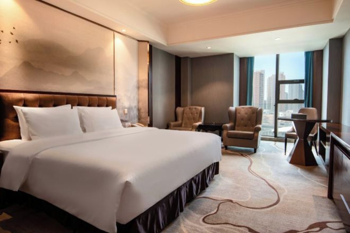 Habitación de hotel con una cama grande, dos sillones, una mesita y vistas a la ciudad.