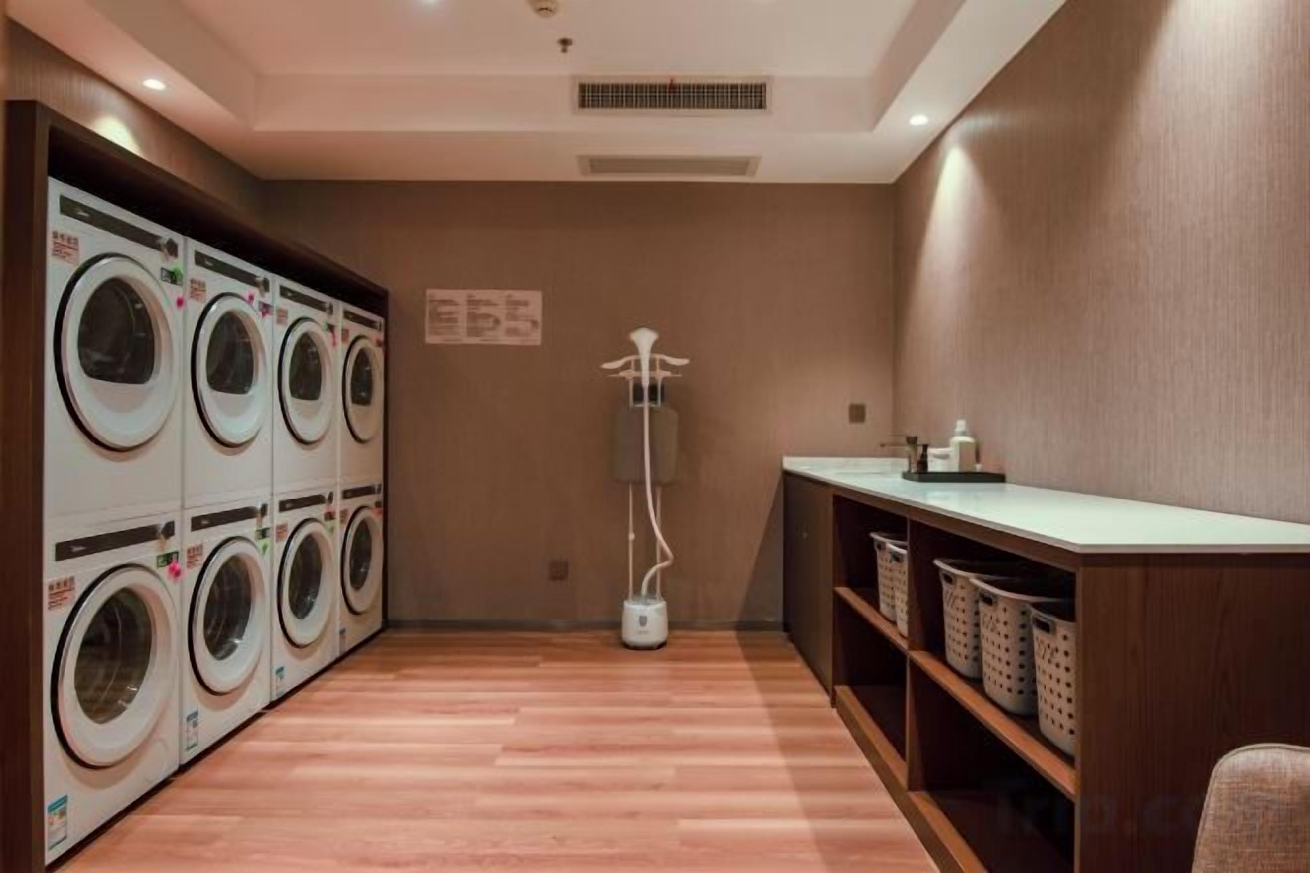A laundry room with multiple washing machines, a floor lamp, and shelves with baskets.