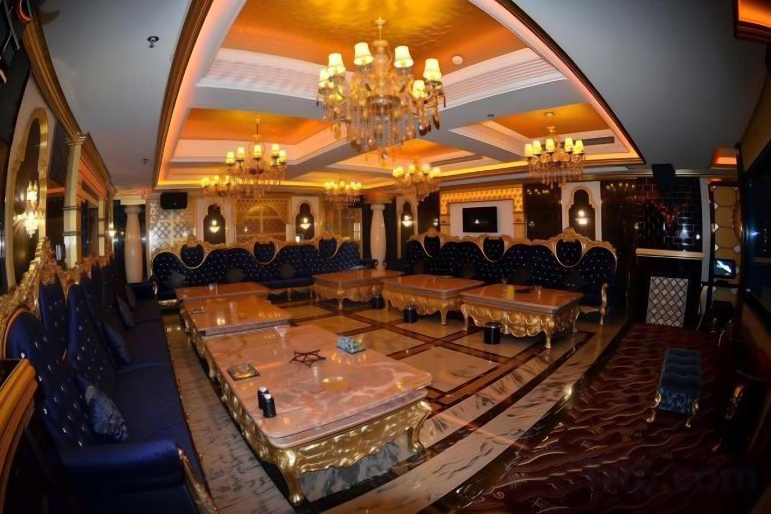 Un salon luxueux doté d’une grande table centrale, de plusieurs espaces de détente et de magnifiques lustres.