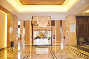 Un hall de hotel con mostrador de recepción, una separadora decorativa y una zona de estar.