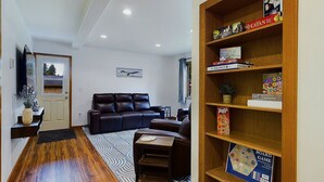 A living room with a dark leather sofa, a wooden bookshelf, and a patterned rug.