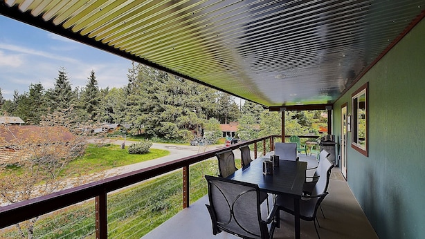 A covered outdoor dining area with a table and chairs, overlooking a green landscape with trees and a road.