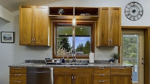 A modern kitchen with wooden cabinets, a stainless steel dishwasher, a large window, and a clock on the wall.