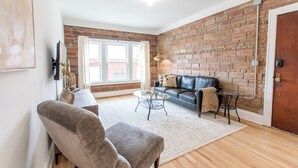 A living room with a brick wall, a leather sofa, a glass coffee table, and a wooden floor. - Modern Loft in Historic Birdtown - Unit 6 (Lakewood)