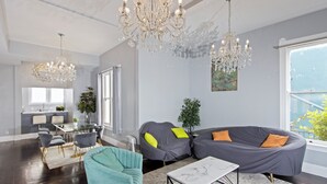 A modern living room with a sectional sofa, a teal armchair, a marble coffee table, and a chandelier.