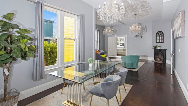 A modern dining area with a glass table, grey upholstered chairs, and a chandelier.