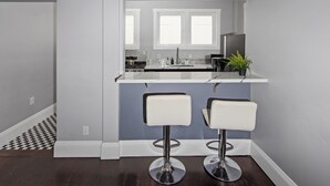A kitchen with two white bar stools, a window, and a countertop with a plant.