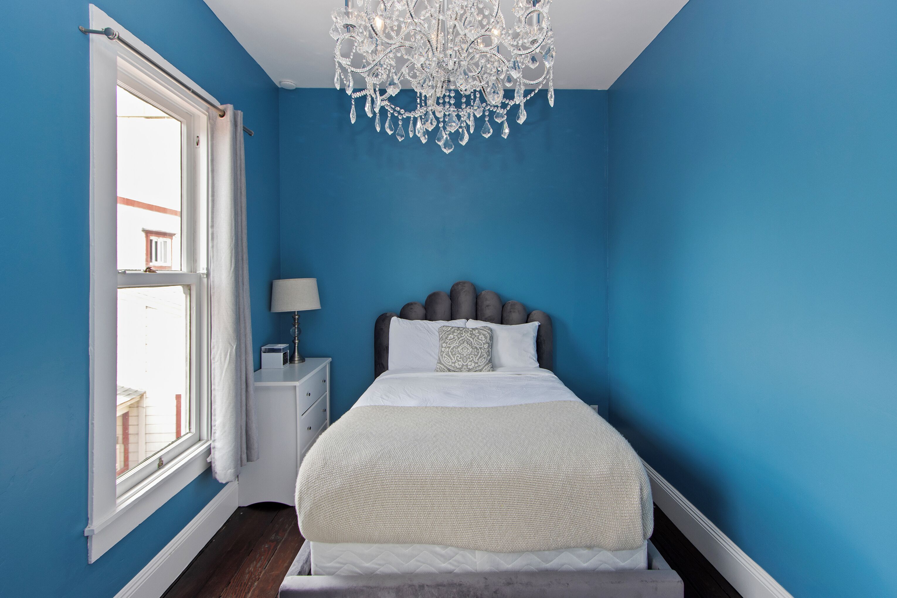 A bedroom with a large bed, a chandelier, a nightstand, and a window with curtains.