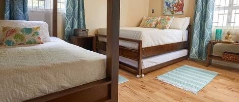 A bedroom with two wooden beds, a window with curtains, an air conditioning unit, and a painting on the wall.