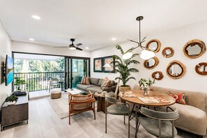 A modern living room with a sofa, dining table, chairs, a ceiling fan, and a balcony with a view. - Park Shore Resort-BLDGC#218*Amazingly remodeled* (Park Shore Resort)