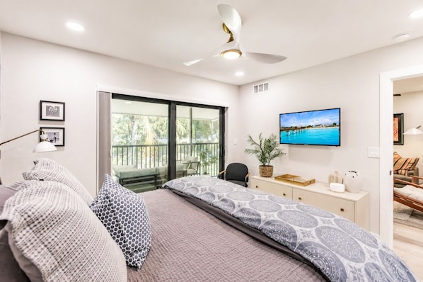 Un dormitorio moderno con una cama grande, televisor, escritorio y balcón con vistas.
