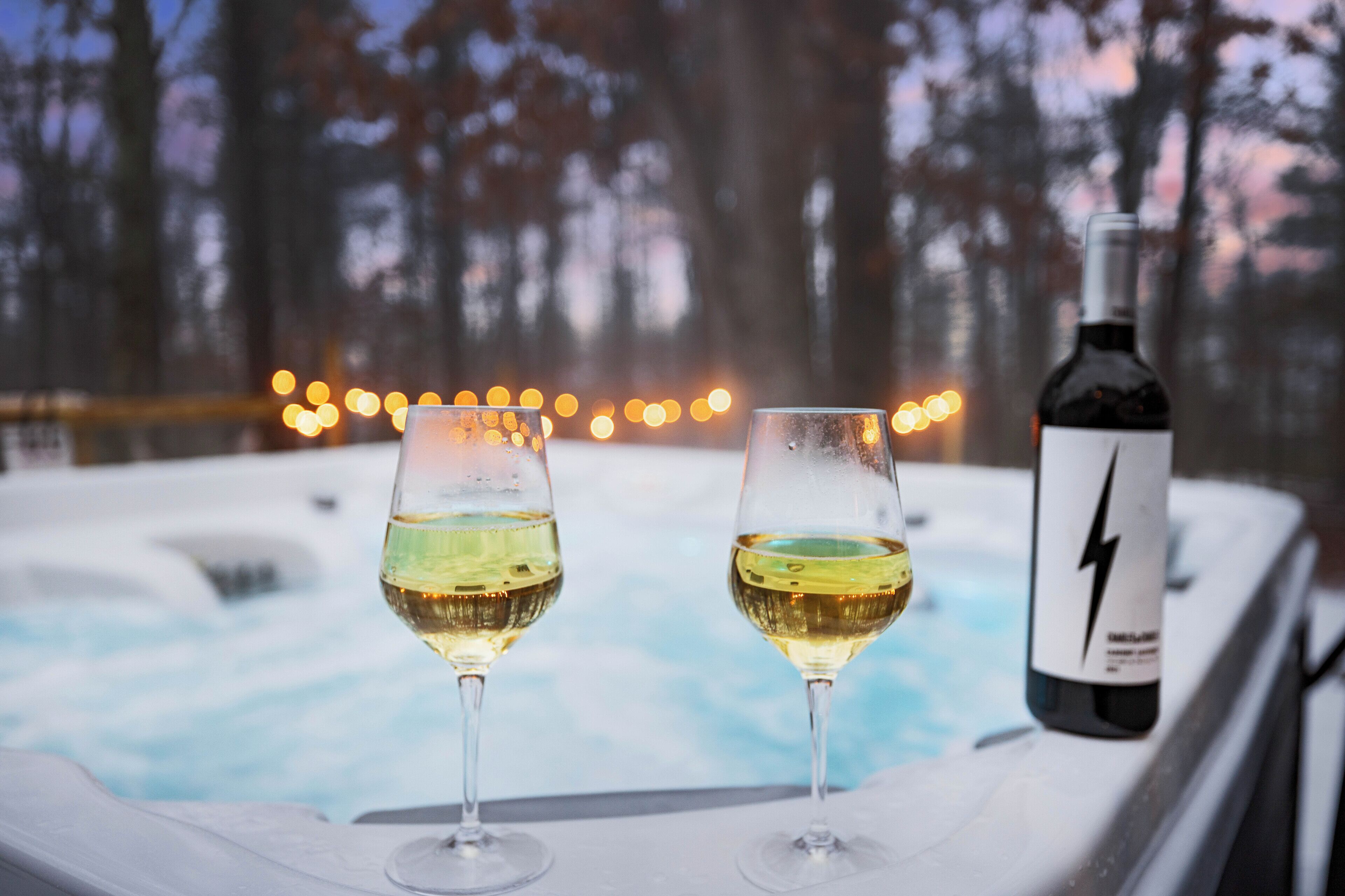 Twee glazen witte wijn bij een hottub, met een fles wijn ernaast.