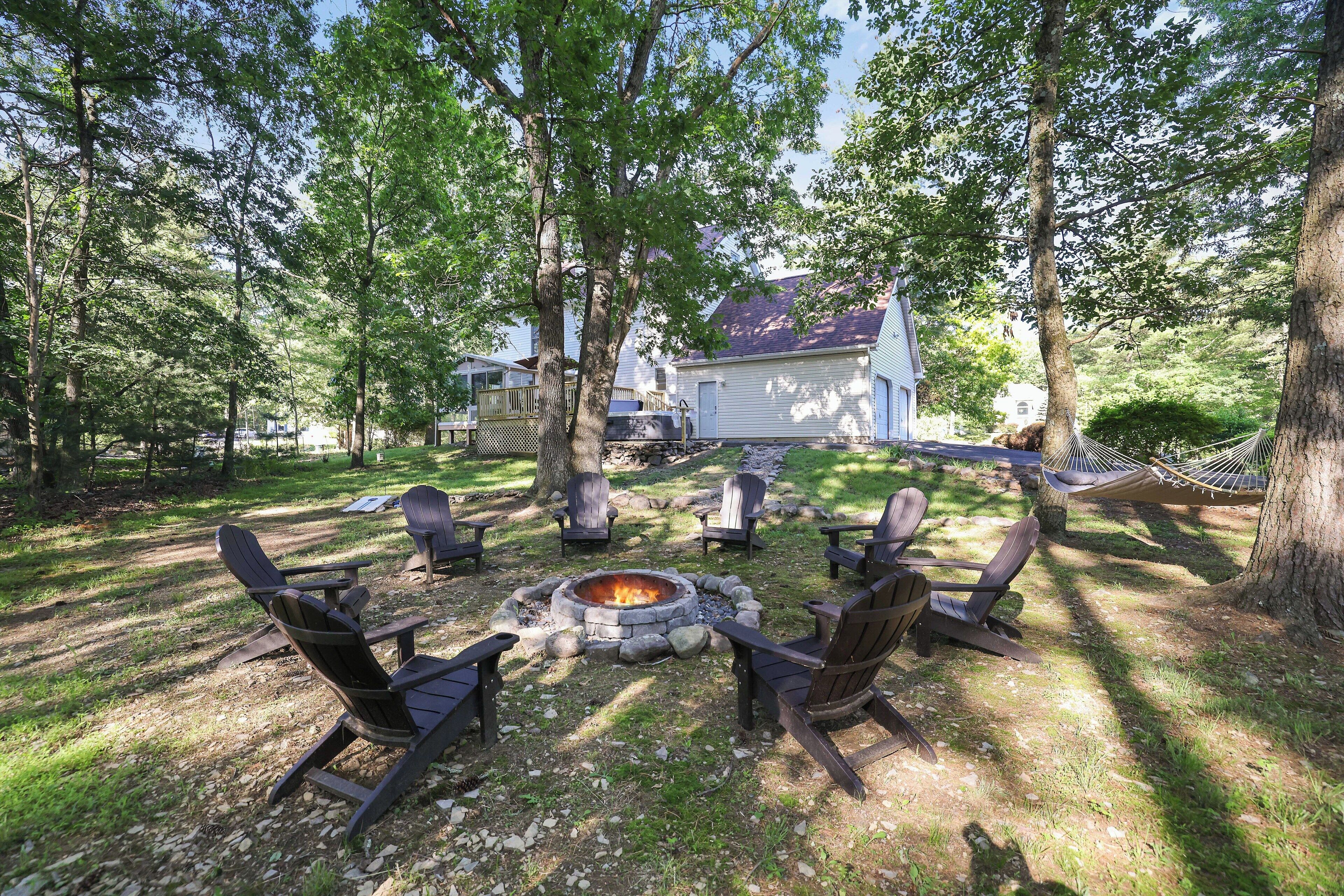 Un jardin avec un foyer en pierre entouré de fauteuils Adirondack, un hamac et une maison en arrière-plan.