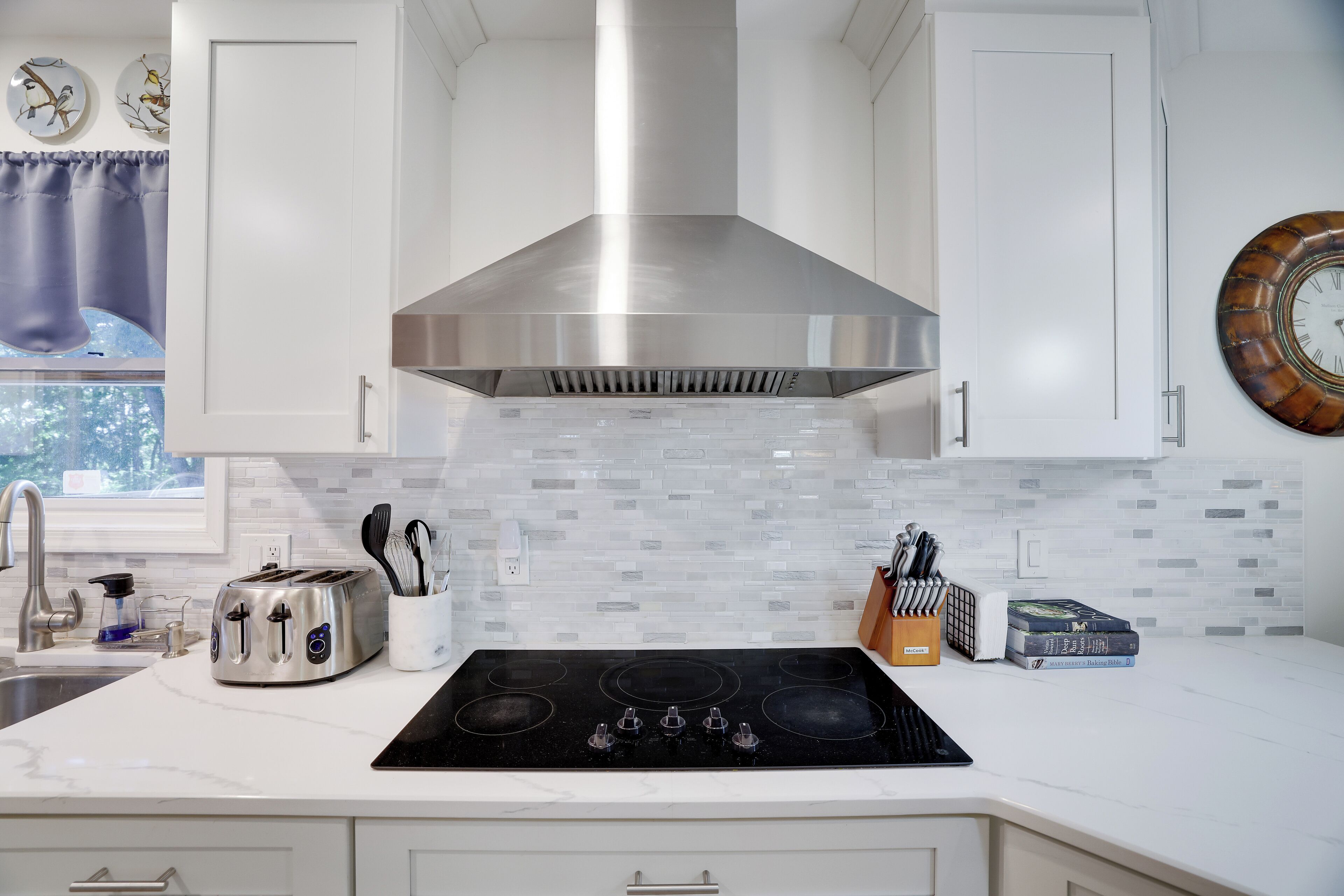 A kitchen with white cabinets, a stainless steel range hood, a black stove, and a window with a view of trees.