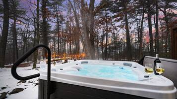 A hot tub in a forested area with a view of trees and a sunset.