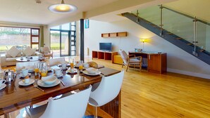 A modern dining area with a wooden table set for breakfast, a sofa, and a TV in the background. - Castlemartyr Holiday Lodges No 3 (2 Bed) (Castlemartyr)