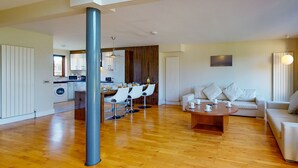 A modern living room with a wooden floor, a dining area with white chairs, and a sofa with cushions. - Castlemartyr Holiday Lodges No 3 (2 Bed) (Castlemartyr)