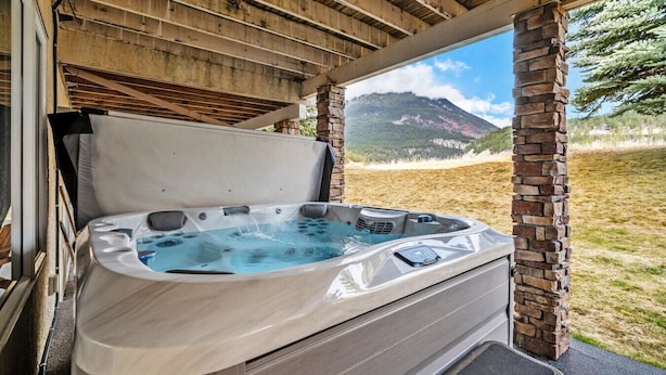 A hot tub under a wooden pergola with a mountain view.