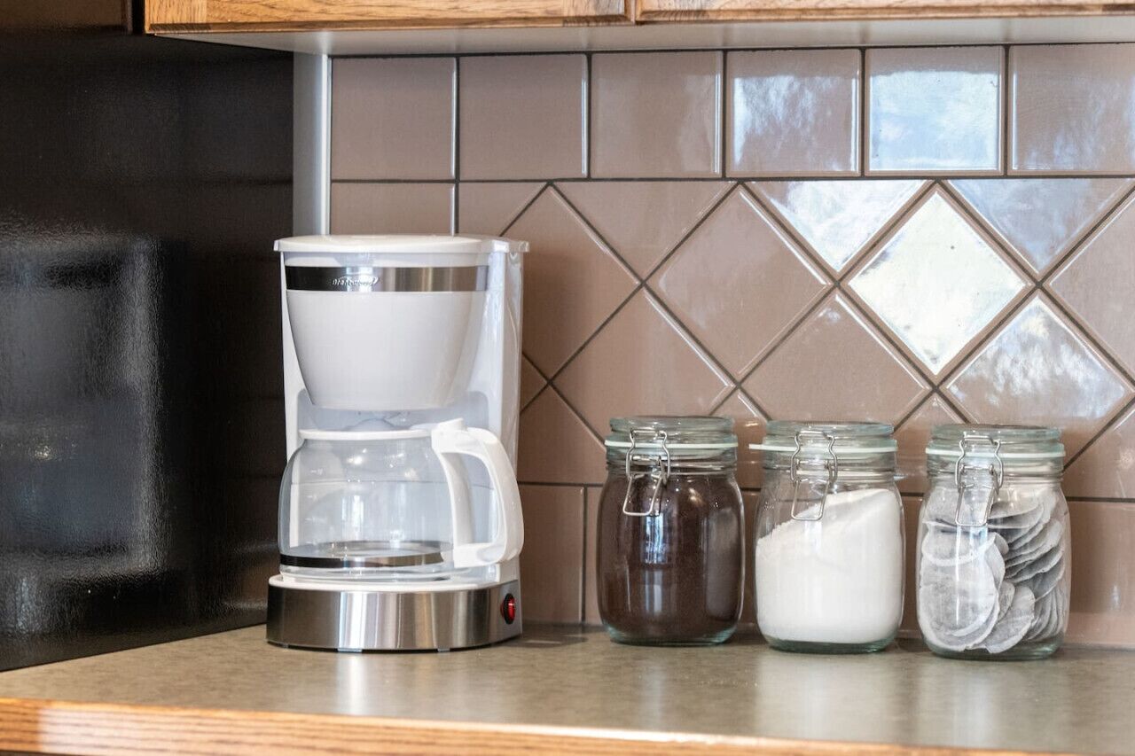 Une cuisine équipée d’une machine à café, de pots à sucre et de différentes épices disposés sur le plan de travail.