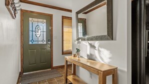 A clean, modern entryway with a green door, a wooden console table, and a black refrigerator.