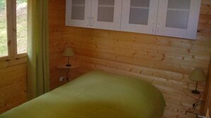 A wooden cabin room with a bed, a window with curtains, and a wall-mounted cabinet.