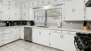 A modern kitchen with white cabinets, a stainless steel sink, a dishwasher, a stove, and a microwave.