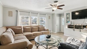 A living room with a beige sectional sofa, a glass coffee table, a ceiling fan, and a mounted TV.