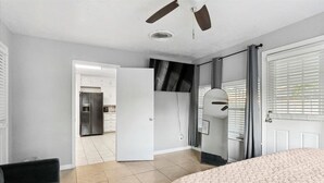 A bedroom with a bed, a ceiling fan, a door leading to a bathroom, and a view of a kitchen.
