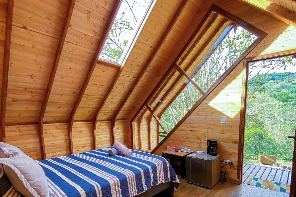 Une chambre mansardée chaleureuse avec un plafond en pente en bois, un lit recouvert d’une couvre-lit à rayures, une petite table et une table de chevet.