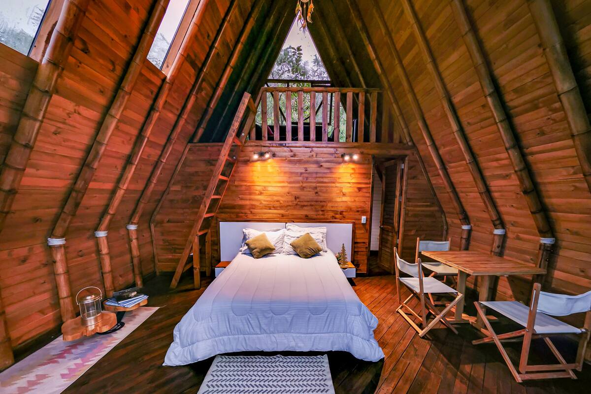 Une chambre mansardée chaleureuse, aux murs lambrissés, comprenant un lit, un coin salon et offrant une vue sur l’extérieur.