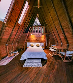 Ein gemütliches Schlafzimmer im Dachgeschoss mit Holzwänden, einem Bett, einer Sitzecke und Blick ins Freie.