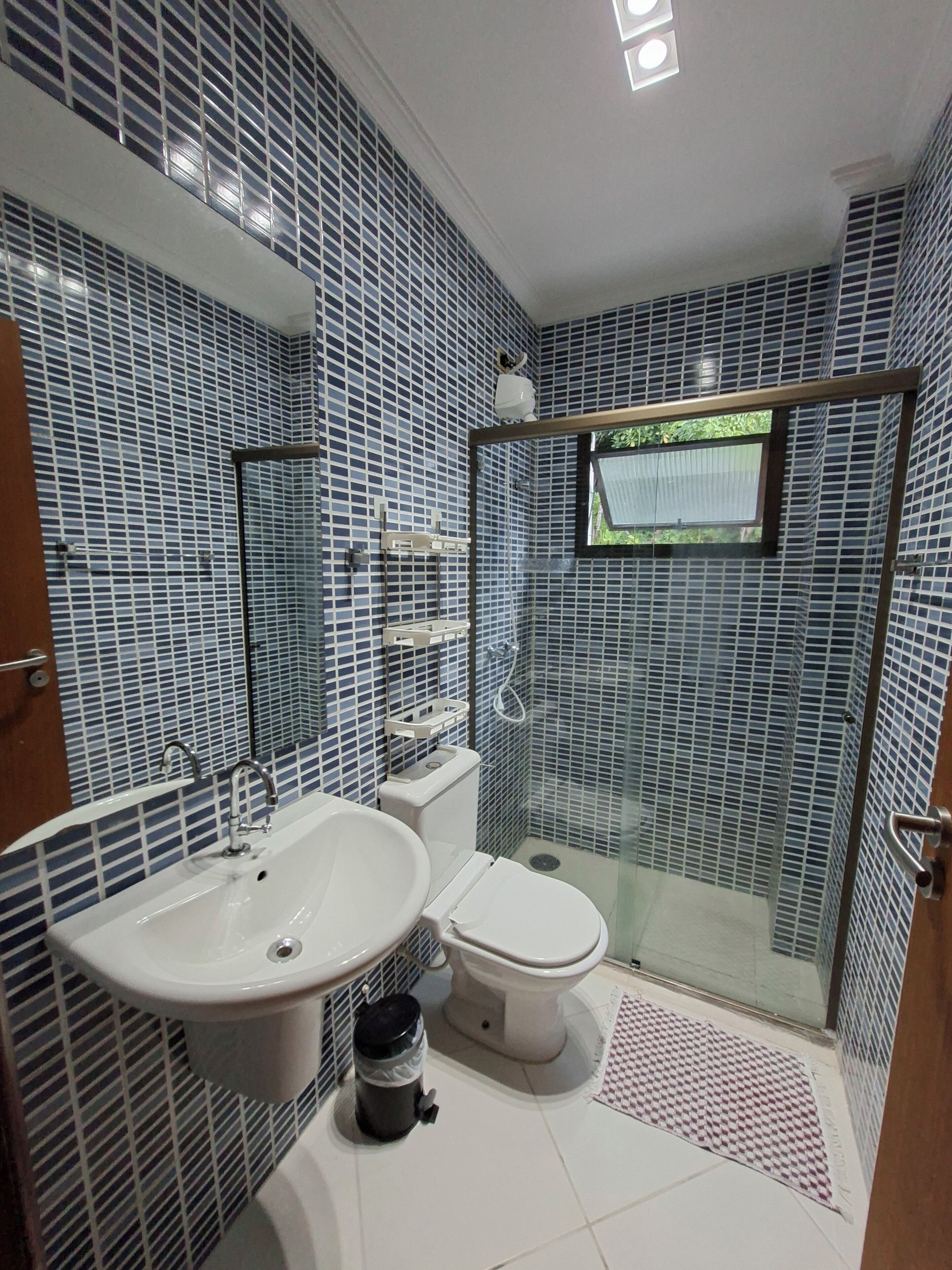 A bathroom with a sink, toilet, and shower area, featuring blue patterned tiles and a glass shower enclosure.