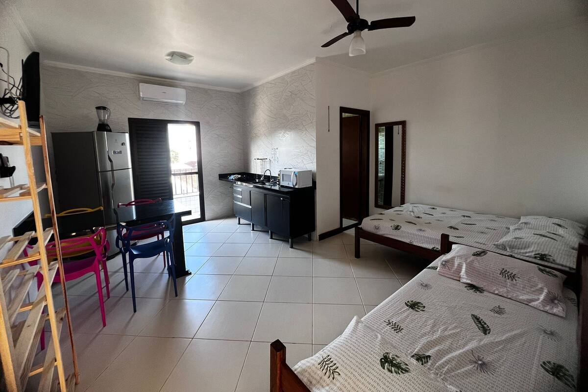 Een compacte kamer met kitchenette, een bed met beddengoed met patroon, een plafondventilator en een raam.