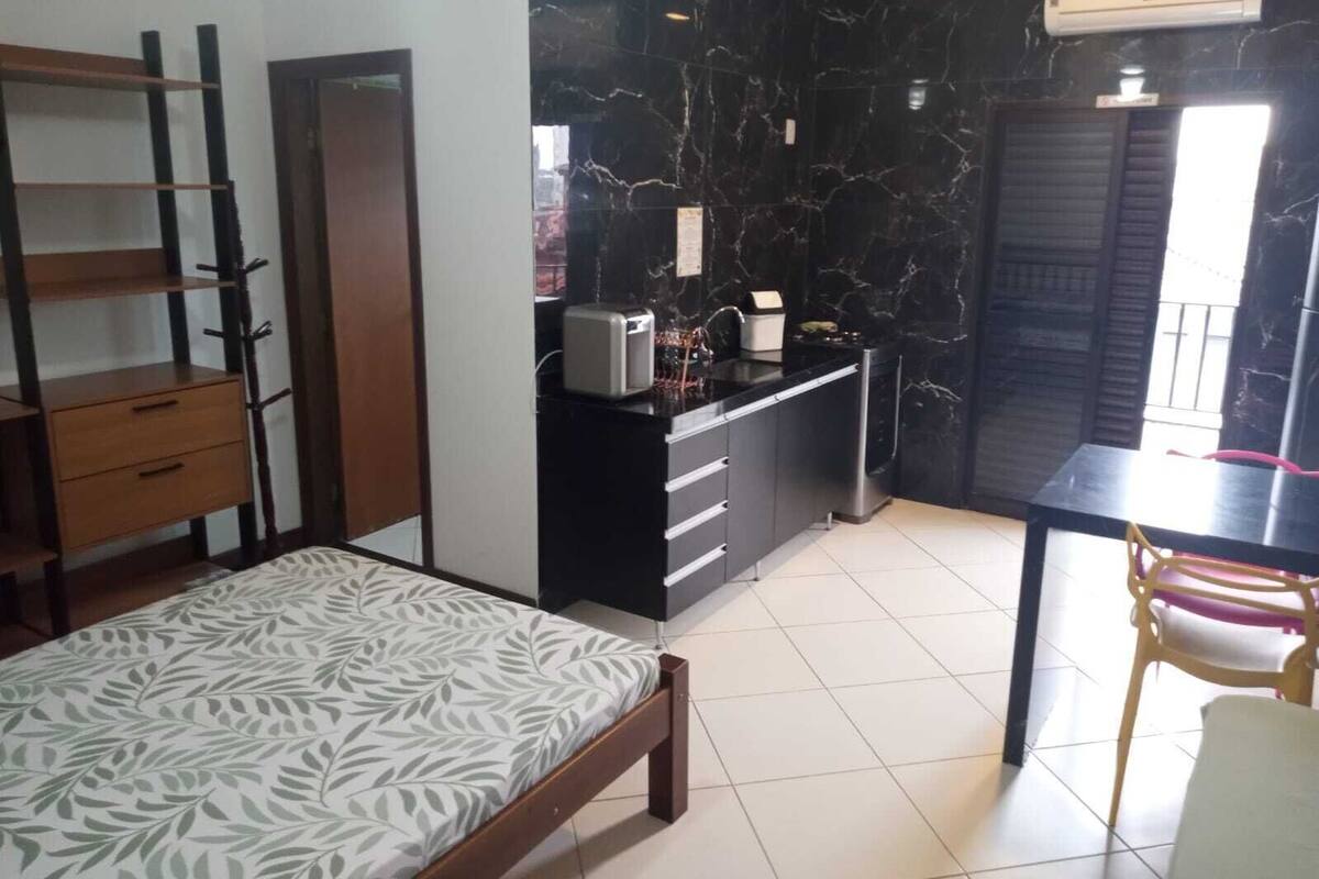 Een knus verblijf met een bed, een kitchenette, een eettafeltje en een stoel.