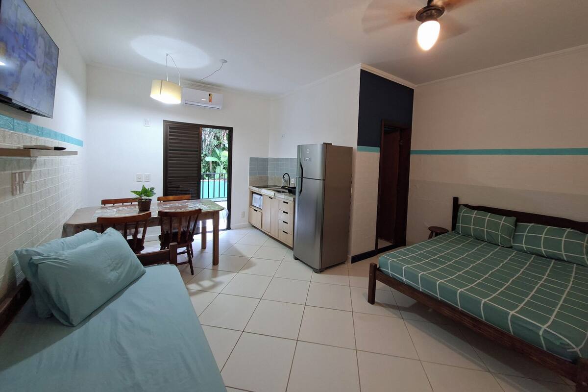 Een compacte leefruimte met een bed, een eettafel met stoelen, een kitchenette en een plafondventilator.