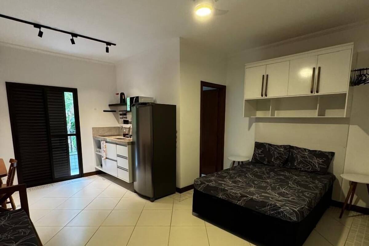 Een slaapkamer met een bed, een plafondventilator, een kledingkast en een kitchenette.