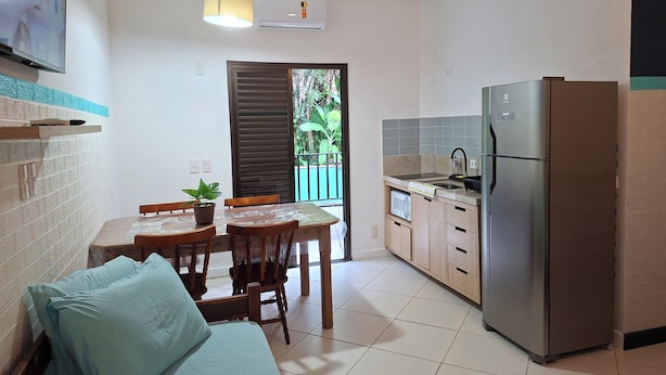 A compact kitchen with a dining area, a refrigerator, and a window overlooking greenery. - Dell Mar Rentals - Flats and Apartments for Season - Ubatuba (Ubatuba)