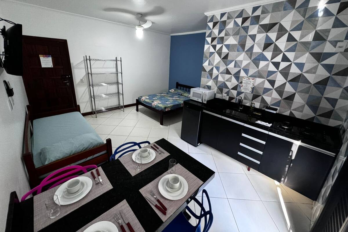 Een compacte kamer met een bed, een kitchenette en een eethoek voor twee personen.