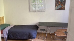 Une petite pièce simple, avec un lit, un bureau, une chaise et une fenêtre ornée de rideaux en dentelle.