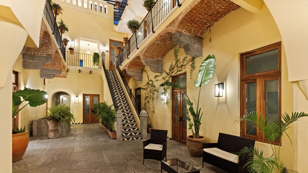 A spacious courtyard with a central staircase, potted plants, wicker furniture, and a brick ceiling. - Casa Haus Hotel Puebla Centro Histórico (Puebla)