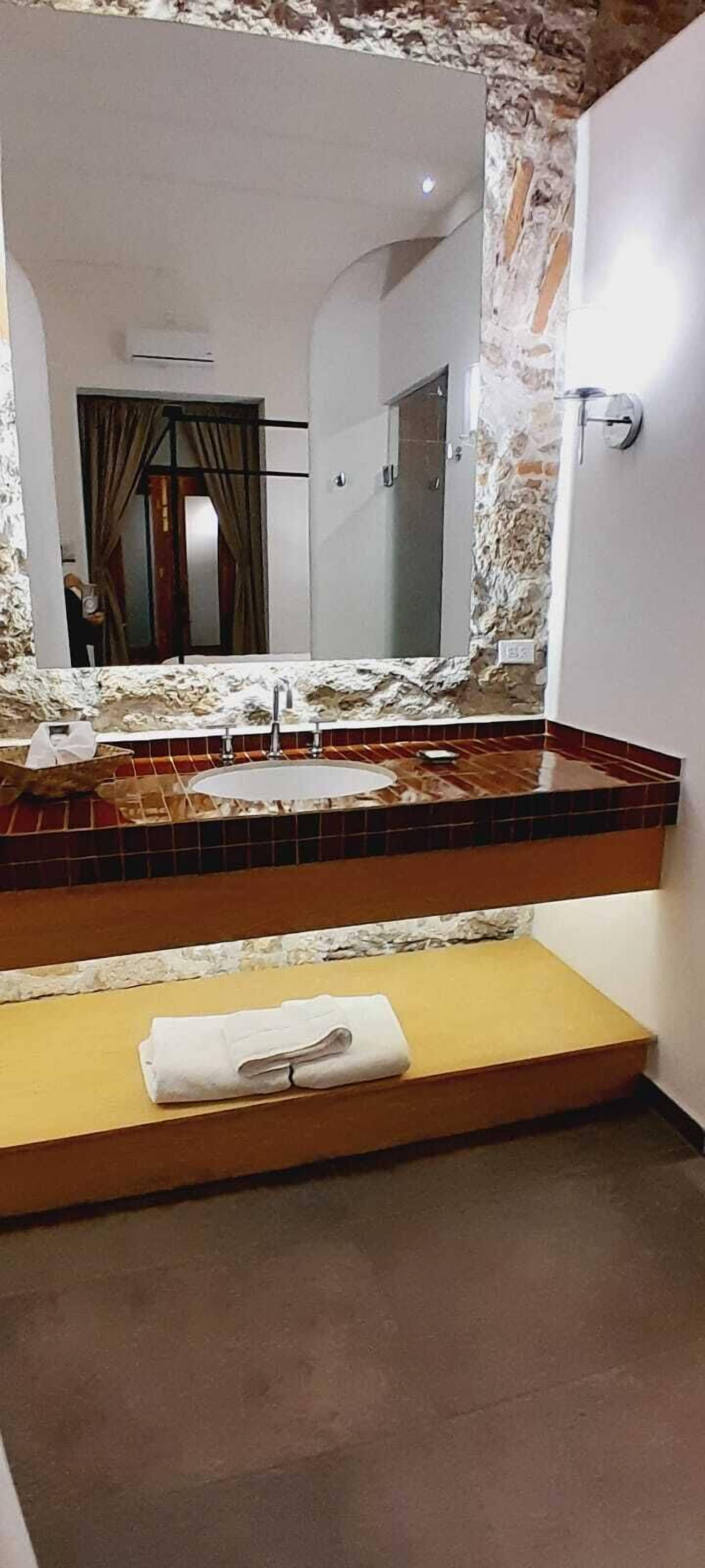 A bathroom with a large mirror, a sink with a marble countertop, and a towel on a wooden shelf.