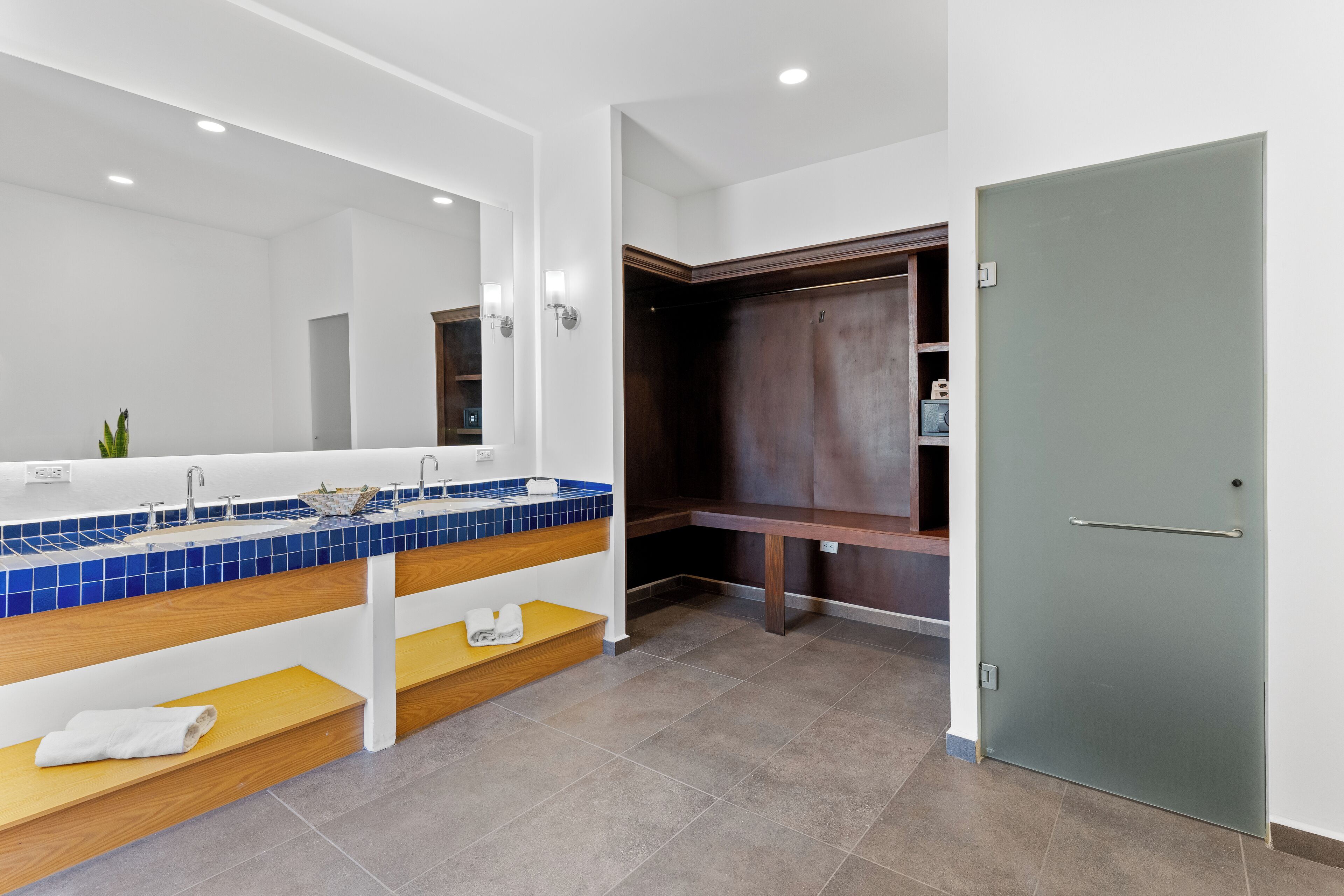 Ein modernes Badezimmer mit einem großen Spiegel, einem blauen Waschbecken mit Fliesen, Holzregalen und einem begehbaren Kleiderschrank.