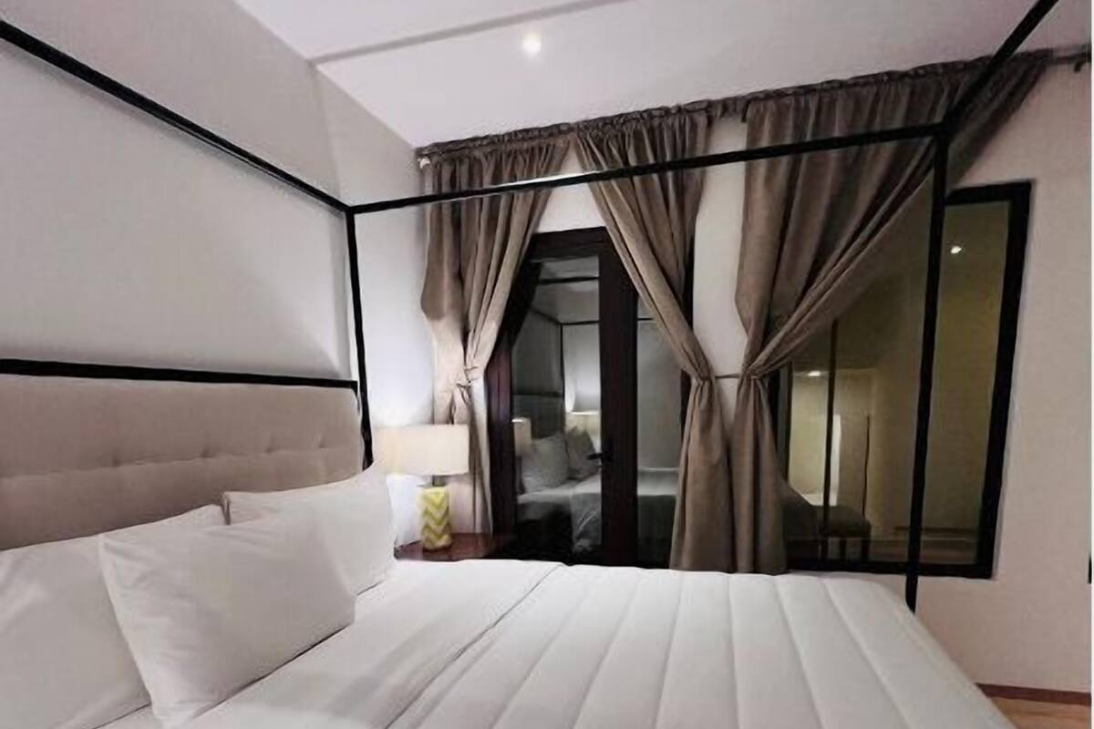 A modern hotel room with a large bed, a nightstand, and a view through a glass door.
