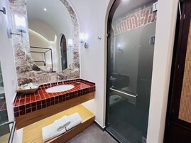 Een badkamer met een wastafel met stenen tegels, een grote spiegel en een douche met glazen wanden.