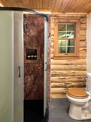 Een badkamer met een rustieke houten wand, een houten raam, een toilet en een douchecabine met een achterwand van steen.