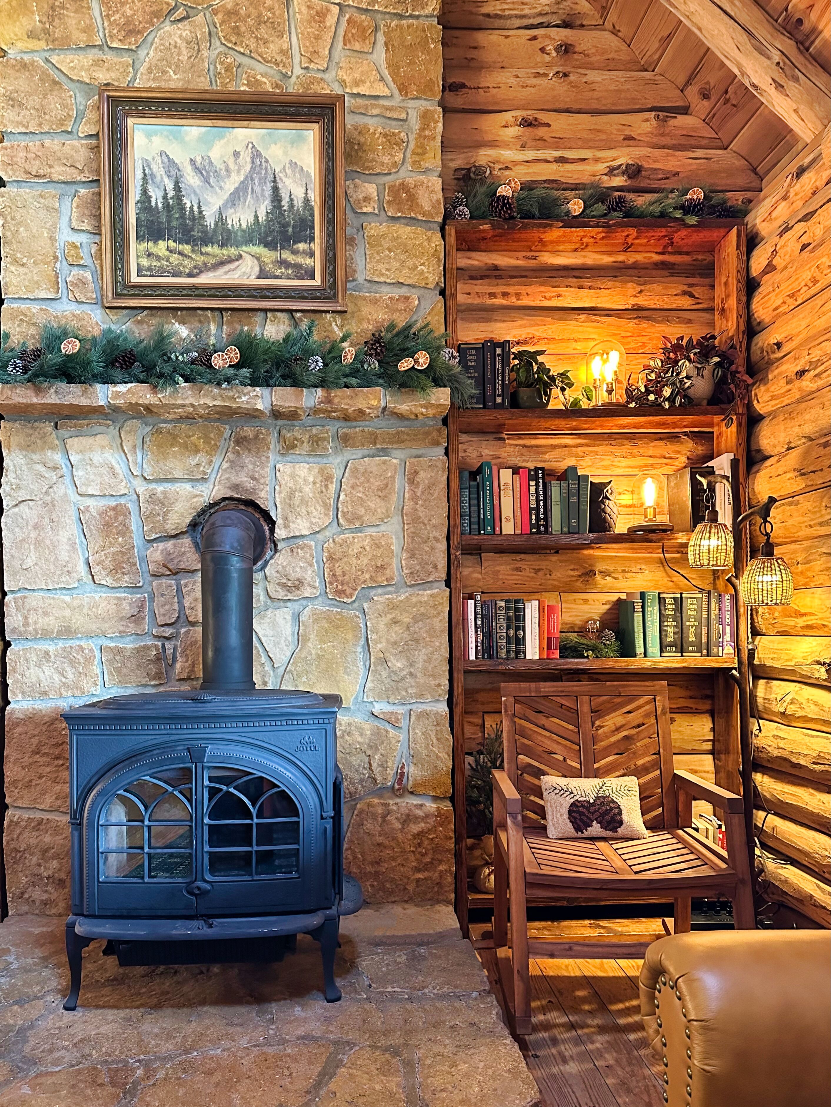 A cozy log cabin interior with a stone fireplace, a bookshelf, and a comfortable seating area.