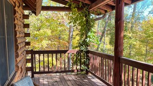 A wooden deck with a glass table and two chairs, overlooking a forest. - Charming log cabin by Berkeley Springs w/ hot tub! (Hedgesville)