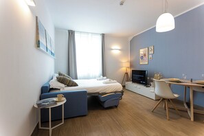 A modern hotel room with a bed, a desk, a chair, a TV, and a small table with a cup and book.