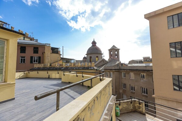 A rooftop terrace with a metal railing, overlooking a historic building with a dome and bell tower.