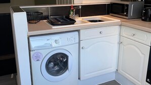 Een kleine keuken met een inbouw wasmachine, een magnetron en een spoelbak.